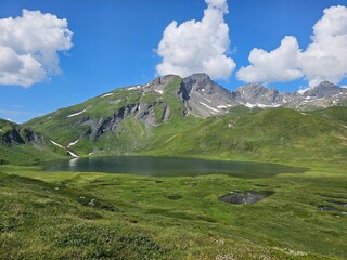 La Thuile, Val D'Aosta, July 02 2025: Panoramic view to the alps, beautiful green landscape reflected in a small natural lake. Beautiful blue sky with some clouds. Mountains with a little snow. Aerial