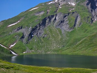 La Thuile, Val D'Aosta, July 02 2025: Panoramic view to the alps, beautiful green landscape reflected in a small natural lake. Beautiful blue sky with some clouds. Mountains with a little snow. Aerial