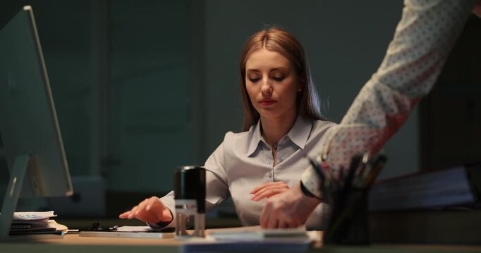 Businessman approaches desk and hands document to woman. Female office worker accepts report and presses stamp firmly onto paper. Slow motion