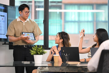 Team brainstorming user interface project while colleague raises hand to ask a question