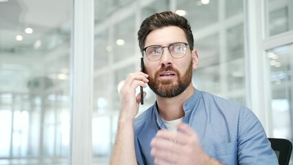 Confident businessman talking on mobile phone while sitting at workplace in modern office. Manager communicates with a client or has a conversation with a business partner using a smartphone. Close up - Powered by Adobe