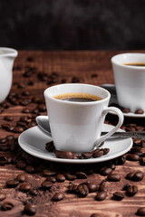 A cup of dark roasted coffee on a white saucer, surrounded by coffee beans on a brown wooden surface