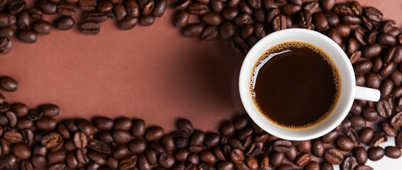 A espresso cup filled with dark coffee surrounded by roasted beans. Banner. Copy space.