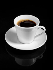 A steaming cup of dark roast coffee sits on a white saucer against a stark black background.