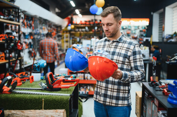 Shopping in hardware store. Man during shopping chooses protective hard hat in hypermarket of building materials.