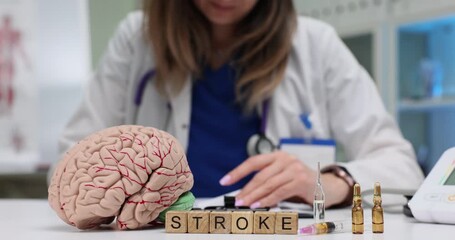 Female doctor focused on papers near Stroke on blocks by brain model and medical vials on desk. Importance of awareness of neurological health