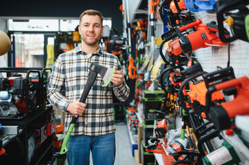 A young man chooses axe in the hardware store