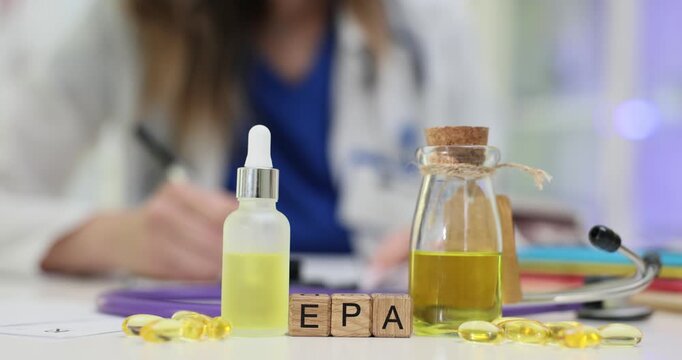 Wooden cubes show EPA referring to essential fatty acid topic. Glass bottle with yellow oil on doctor desk emphasizes nutrition research focus