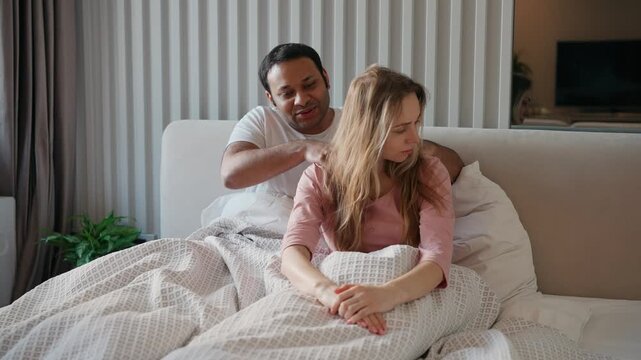 A man massages the shoulders of a pregnant woman while they sit in bed and talk