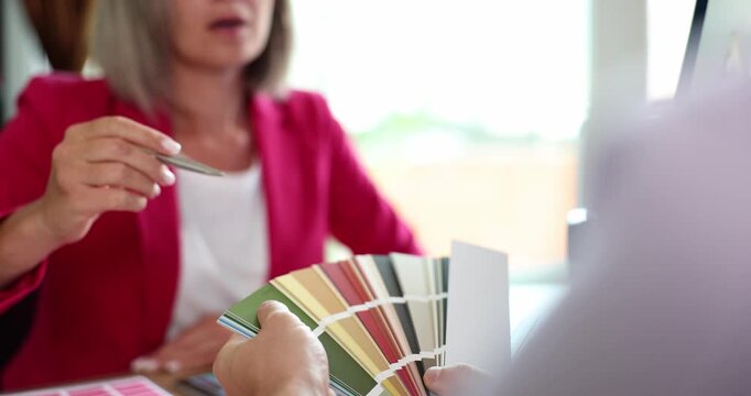 People discuss palettes holding fan of color swatches pointing to item. Collaborative design process involving interior decorating and graphic design