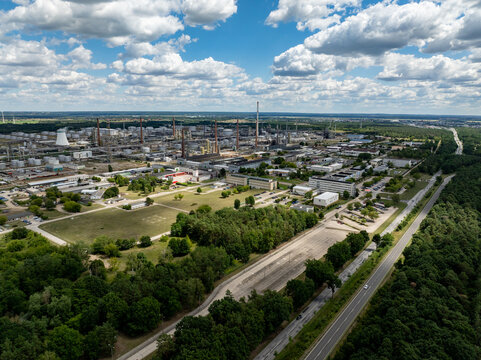 Aerial view of sprawling industrial complex with towering chimneys and metallic structures contrasting with the surrounding verdant trees and open spaces, Schwedt/Oder, Brandenburg, Germany.