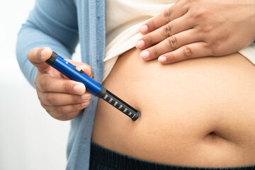 Asian woman injecting herself diabetes injecting insulin in stomach at home.