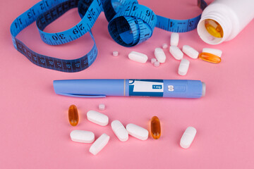 Overhead shot of semaglutide pens, blue measuring tape, and white pill jar on pink table,...