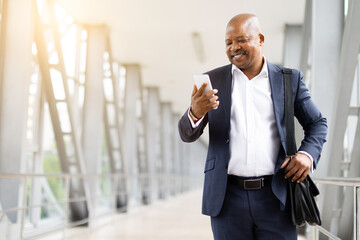 Smiling African American businessman in suit using smartphone while traveling through airport terminal. Concept of communication, mobility and corporate lifestyle, copy space