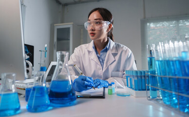 Scientist taking notes while examining blue chemical compounds in laboratory