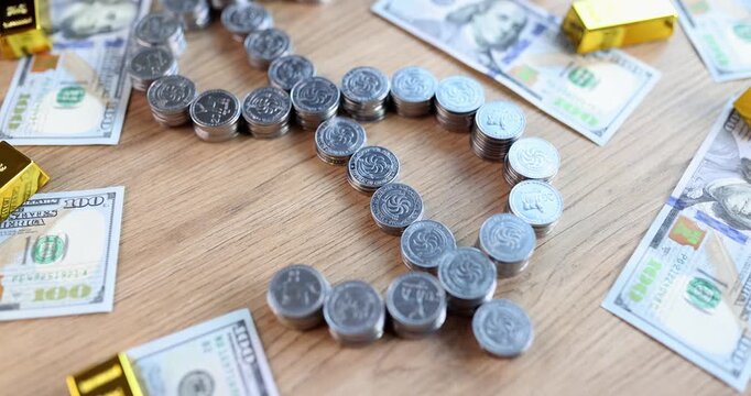 Coins form cross shape of dollar on wooden table surrounded by banknotes and gold bars. Metallic pieces align creating symbolic financial pattern