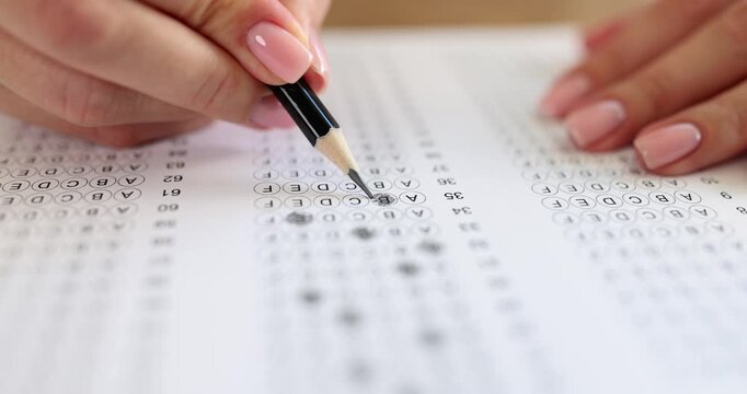 Female hand shades small circle on multiple-choice answer sheet creating marked choice. Pencil tip moves steadily filling blank spot on printed test