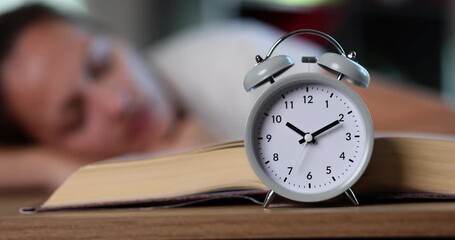Alarm clock stands near open book resting near sleepy student creating wake-up moment. Timepiece shows late hour disturbing learner during quiet nap - Powered by Adobe