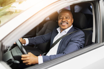 Happy African American businessman driving car, smiling with confidence. Concept of modern lifestyle, transport, success and professional corporate travel journey.