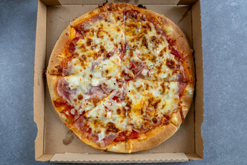 Top view of a freshly baked pizza topped with melted cheese, ham, onions, and tomato sauce inside a cardboard delivery box.