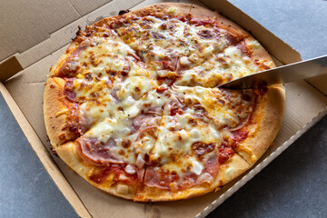 Slicing a freshly baked pizza in a delivery box.