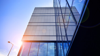 Obraz premium Modern office building with glass facade. Transparent glass wall of office building. Reflection of the blue sky on the facade of the building.