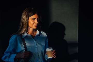Businesswoman drinking coffee walking in the city at dawn