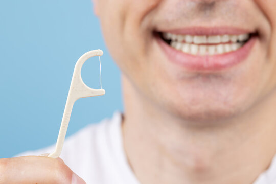Smiling man holding a dental floss pick. Young man with dental floss pick, promoting dental hygiene.