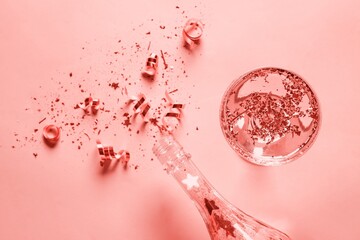 Glass of champagne, bottle and glitters on coral background