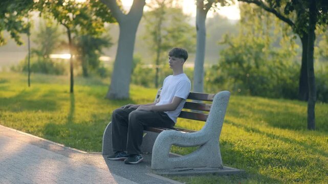 Teen boy chillin solo on park bench in warm summer afternoon light