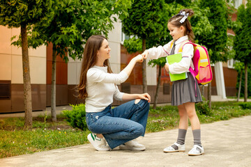 back to school, the mother leads the student's child to the first grade holding his hand, the student girl with her mother and with a backpack goes to school