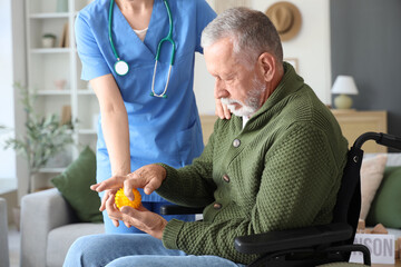 Obraz na płótnie Canvas Senior man suffering from Parkinson syndrome in wheelchair with massage ball and nurse at home