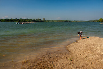 A child is playing by a clear lake with a blue sky background.