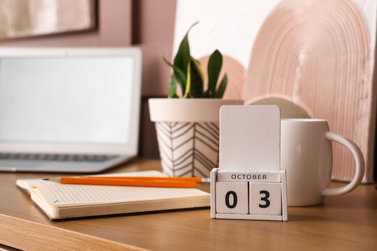 Cube calendar with date 3 October, stationery, modern laptop and houseplant on wooden table