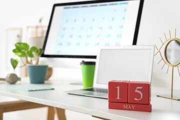 Cube calendar with date 15 May, modern laptop, computer and cup of coffee on table