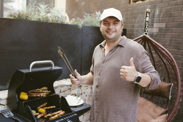 Man grilling sausages and corn on a gas barbecue in backyard. Outdoor cooking, smoke rising, relaxed summer vibe with a hanging chair and cozy terrace setup.