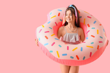 Cute girl with doughnut shaped swim ring on pink background