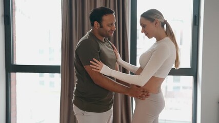 A man kisses a pregnant woman's belly and they hug and hold hands