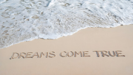 Dreams Come True written in sand as ocean waves approach