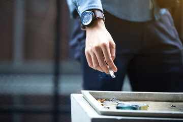 Man hand putting out cigarette on street ashtray, cigarette butt, smoking is dying. Quit smoking. Health concept.