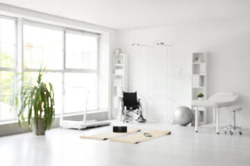 Blurred view of physiotherapist's office with sports equipment, couch and wheelchair