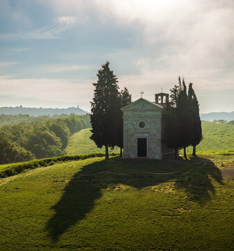 Aerial view of the iconic Cappella della Madonna di Vitaleta standing gracefully amidst rolling green hills, bathed in the soft glow of the Tuscan sun, San Quirico d'Orcia, Tuscany, Italy.