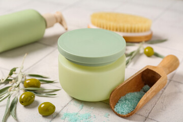 Natural cosmetic products, green olives and massage brush on light tile table