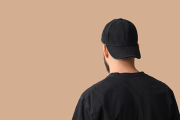 Handsome young man in stylish cap on beige background, back view