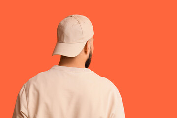 Handsome young man in stylish cap on orange background, back view