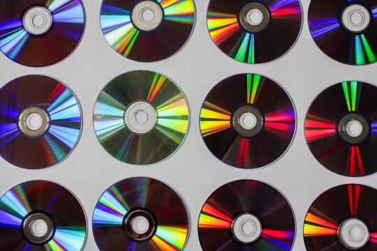 Collection of colorful CD DVD discs arranged in grid pattern with rainbow reflections flatray