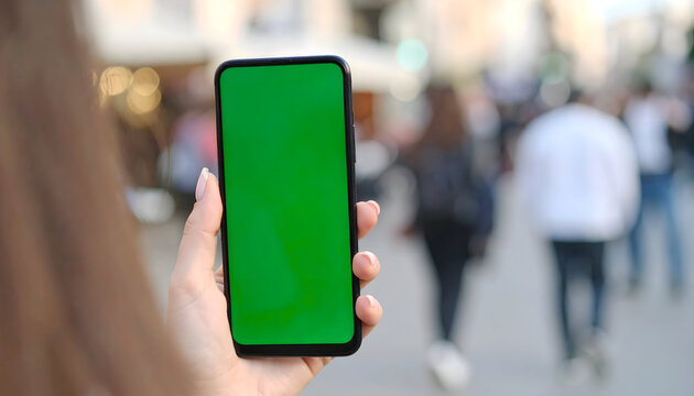 Woman Holding Smartphone With Green Screen Displaying Information Outdoors With Blurred Background