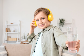 Cute little boy in headphones with glass of water at home