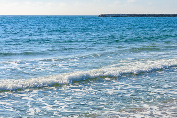 Tranquil ocean waves hitting sandy beach on a sunny day with clear horizon
