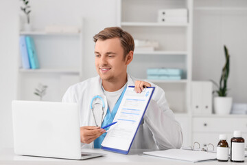 Obraz premium Male doctor with clipboard and laptop giving online consultation in clinic